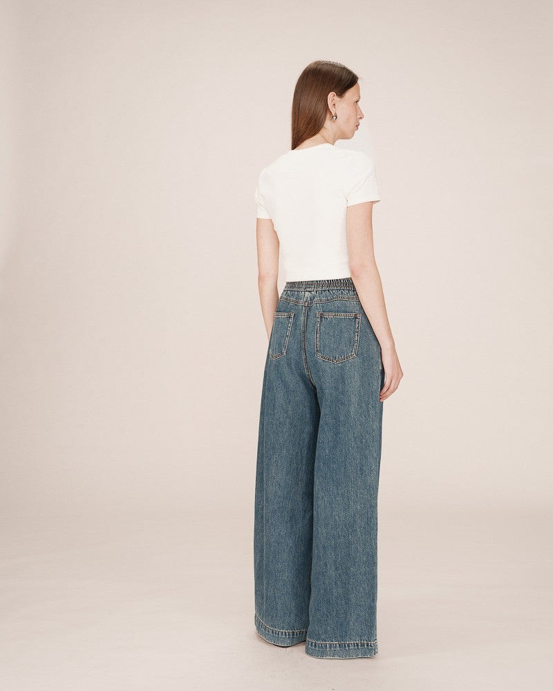 Woman wearing a white t-shirt and blue jeans on a beige background