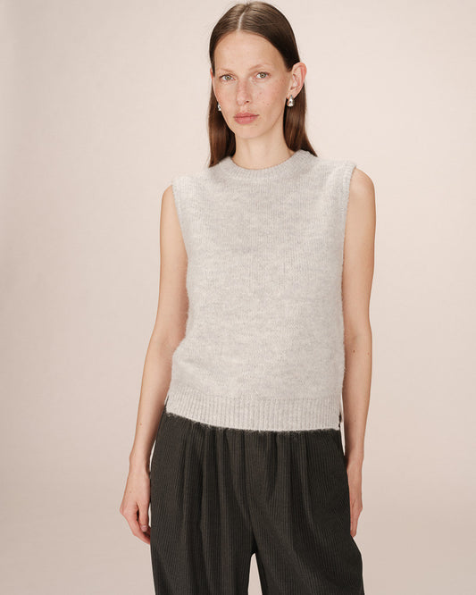 Woman wearing a light gray sleeveless knitted top against a plain background