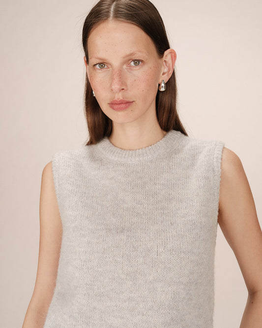 Woman wearing a light gray sleeveless sweater against a plain background