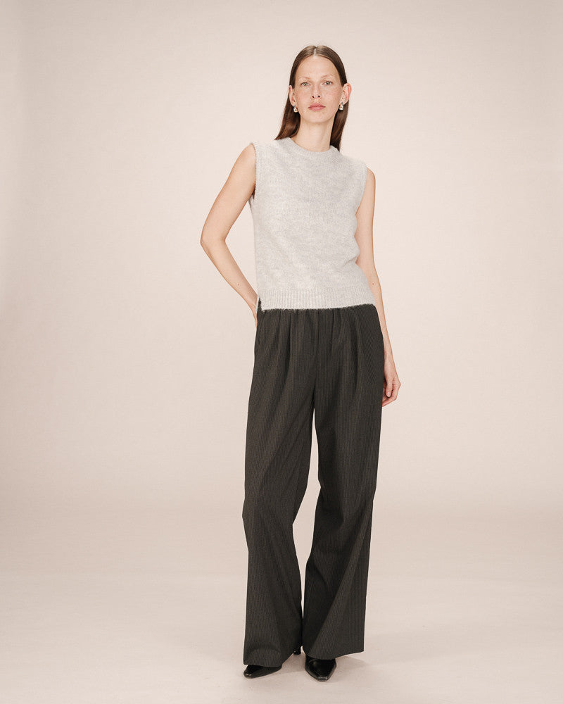 Woman wearing a light gray sleeveless top and black wide-leg pants on a beige background