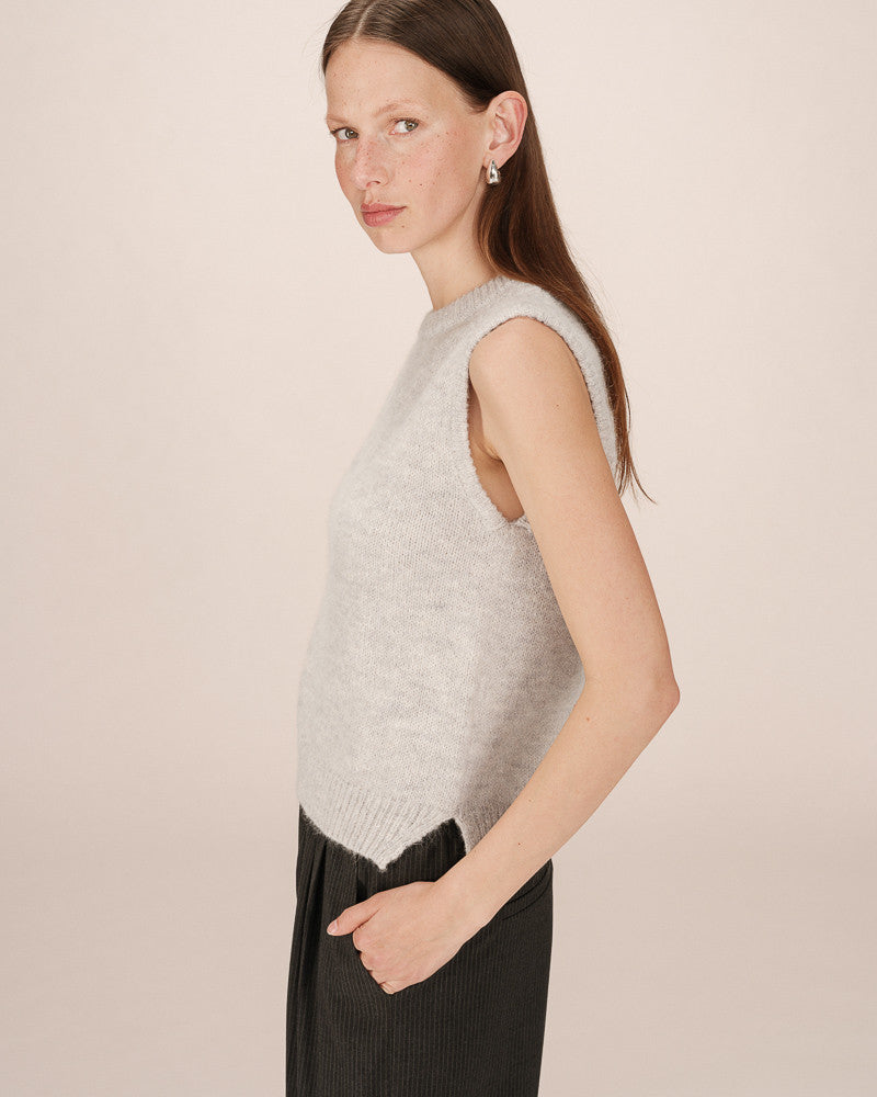 Woman wearing a light gray sleeveless knitted top against a beige background