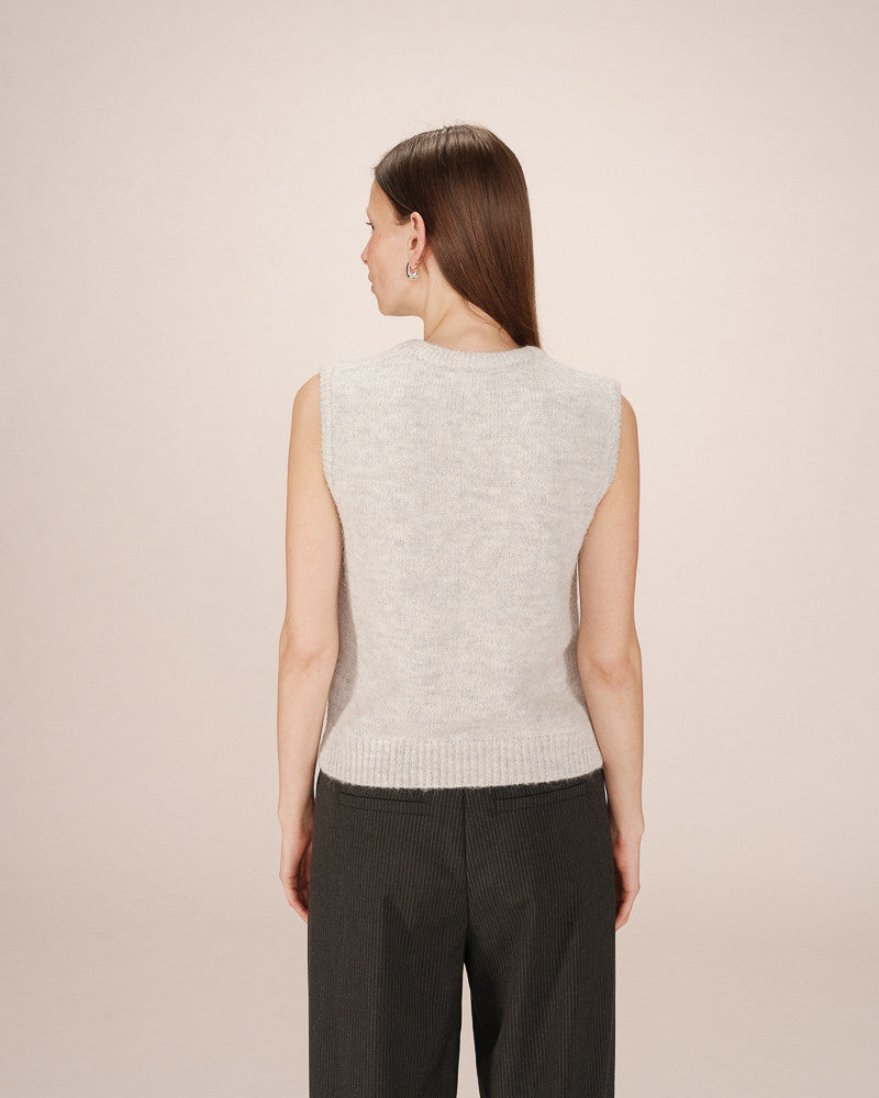 Woman wearing a light gray sleeveless sweater against a beige background
