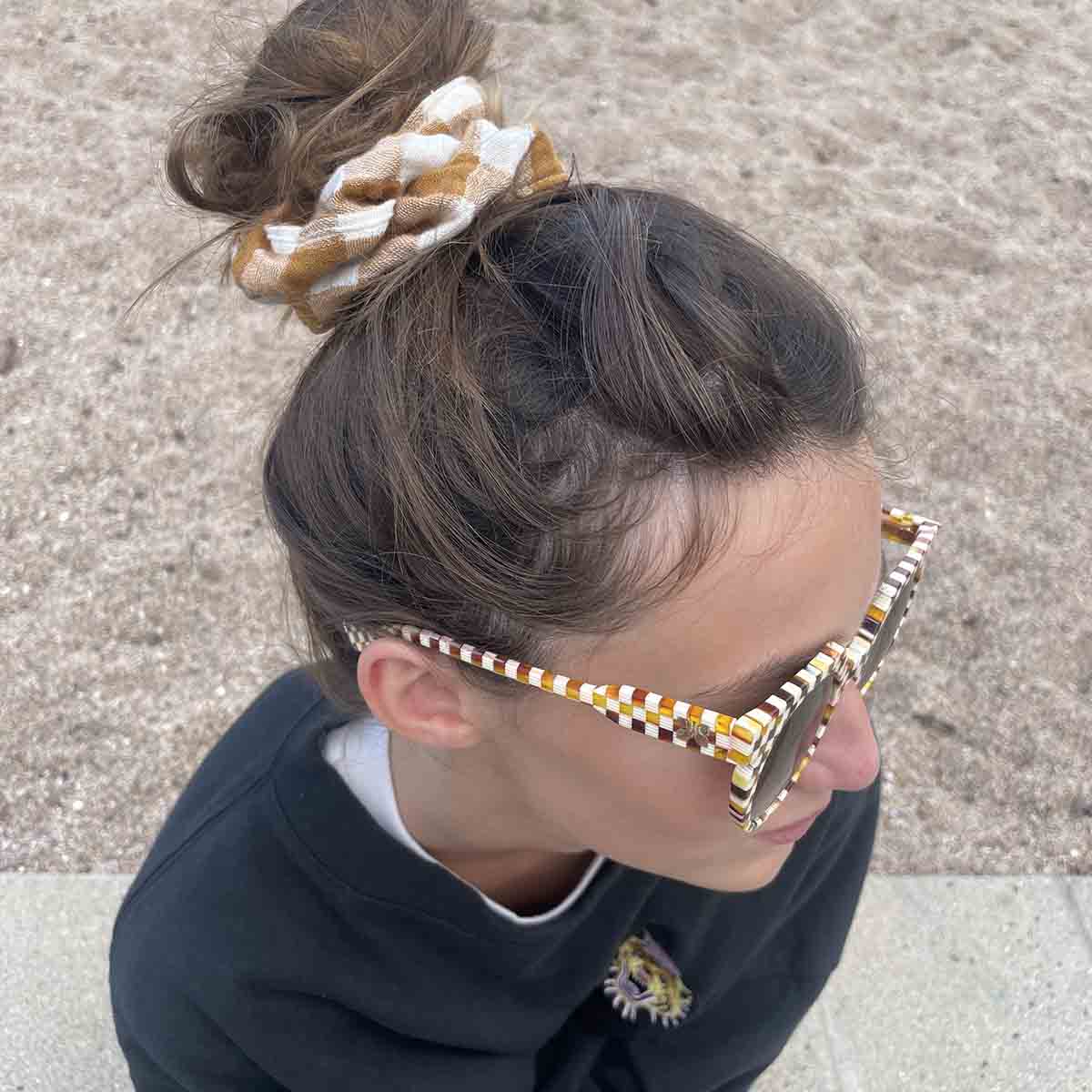 Person wearing gold-framed sunglasses with a textured pattern, sitting on a concrete surface.