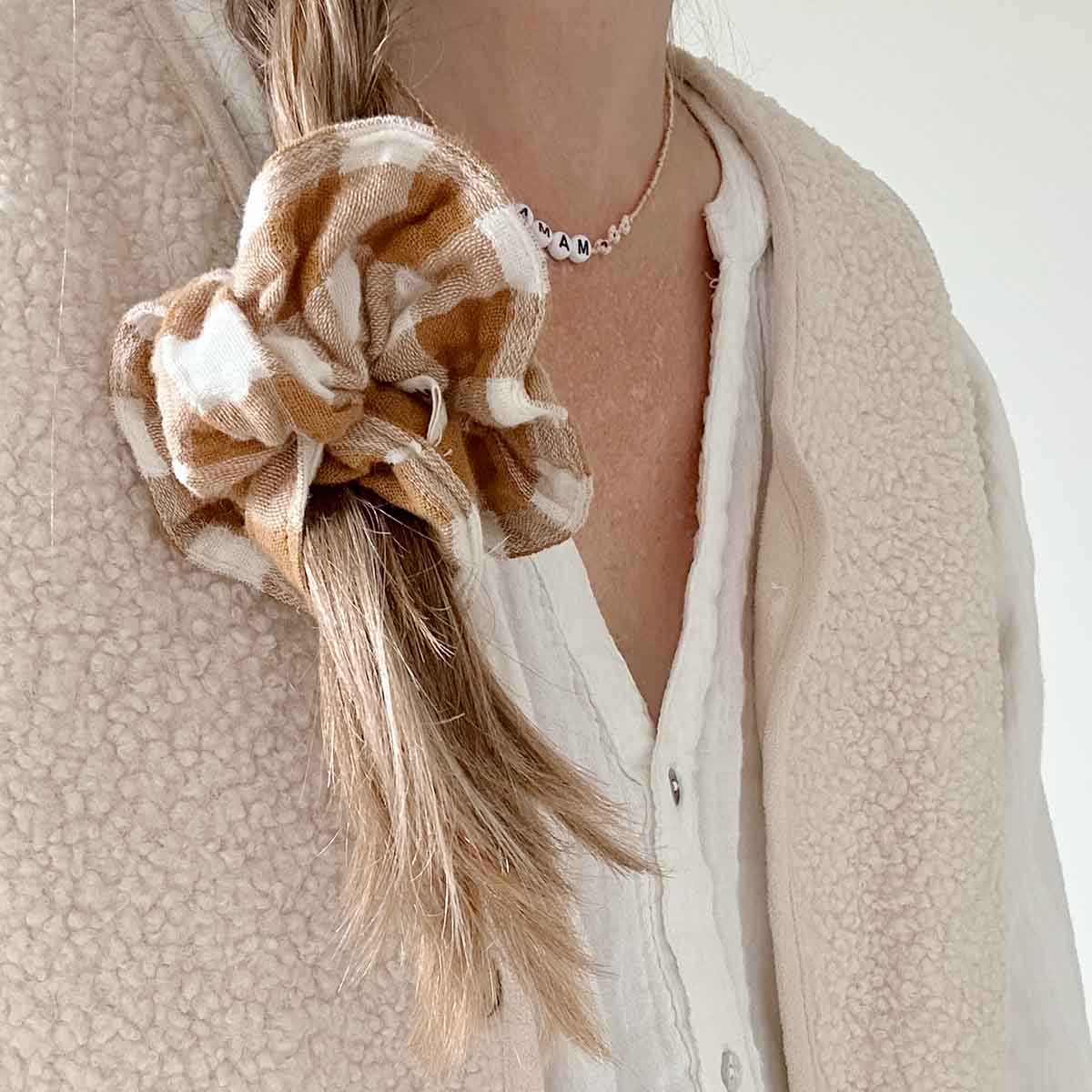Person wearing a beige jacket with a large fabric flower accessory on a neutral background