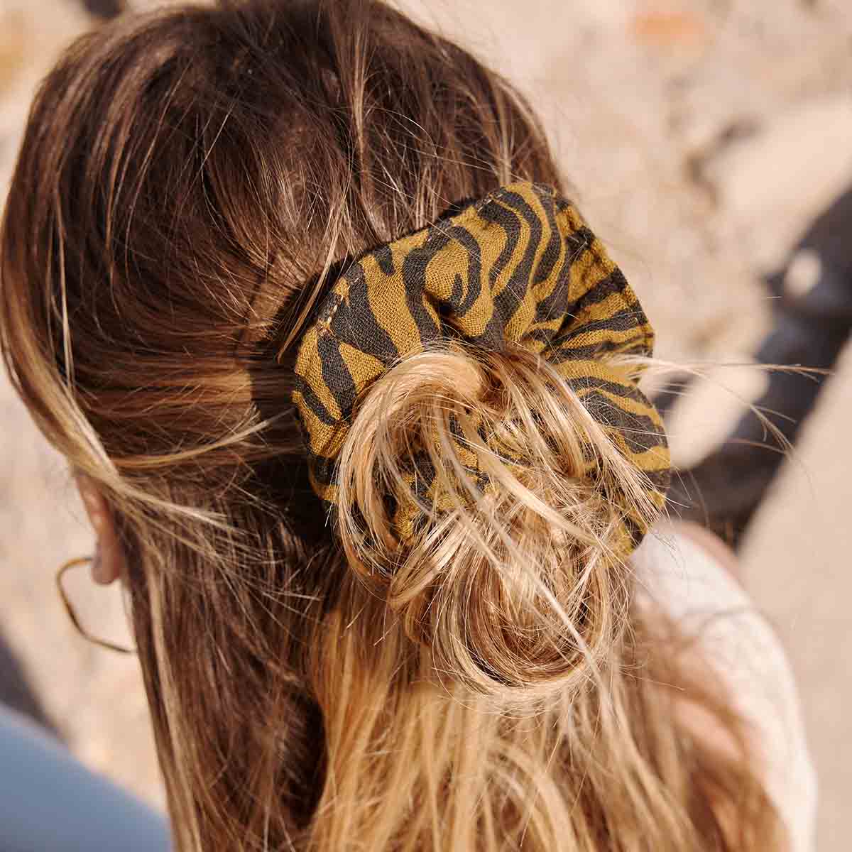 Person with a bun holding a patterned hair tie against a blurred background