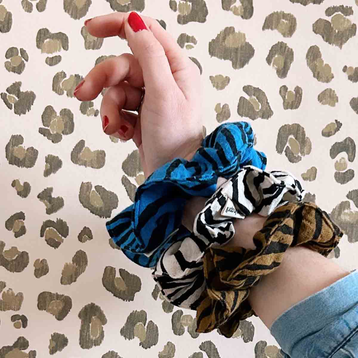 Hand wearing blue scrunchie with patterned scrunchies on a leopard print background