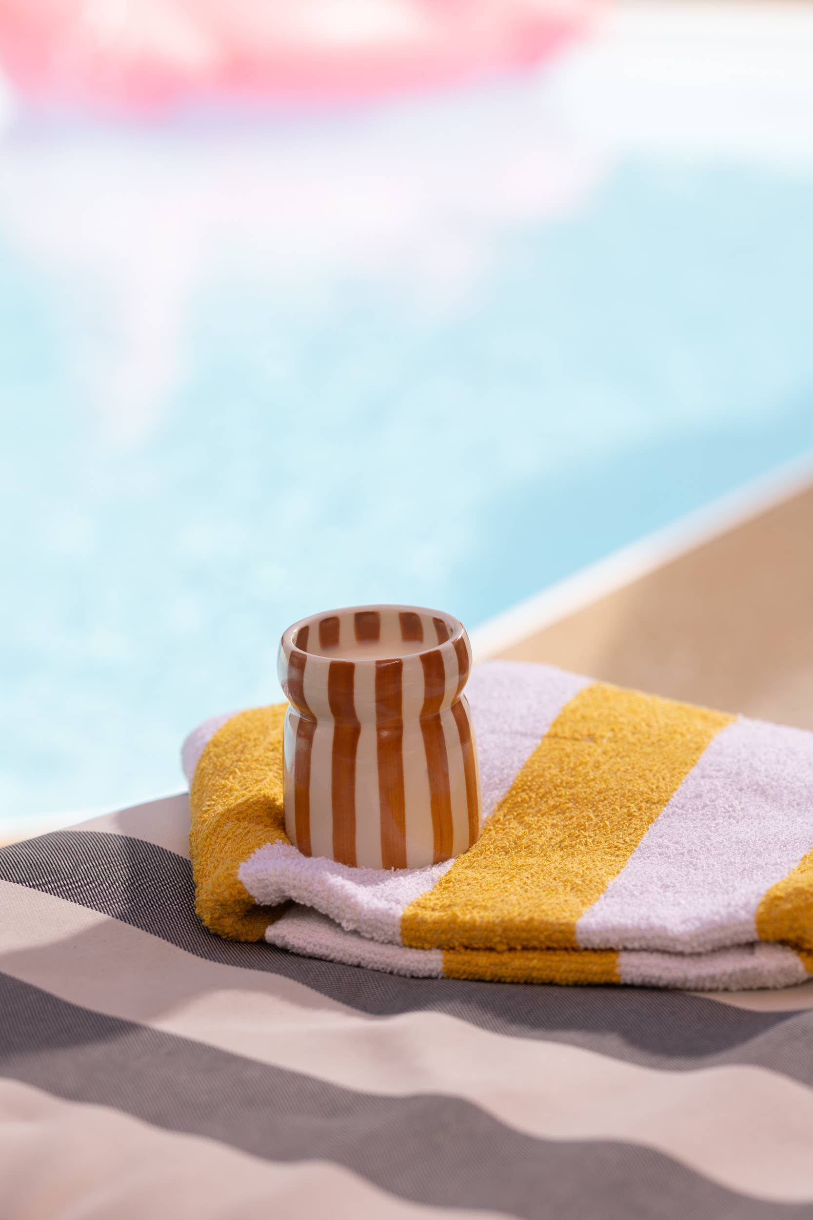Striped towel with a striped container on a sandy surface near water