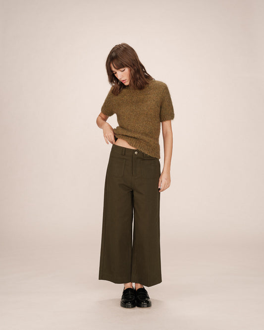 Woman wearing a green knit top and wide-leg pants on a beige background