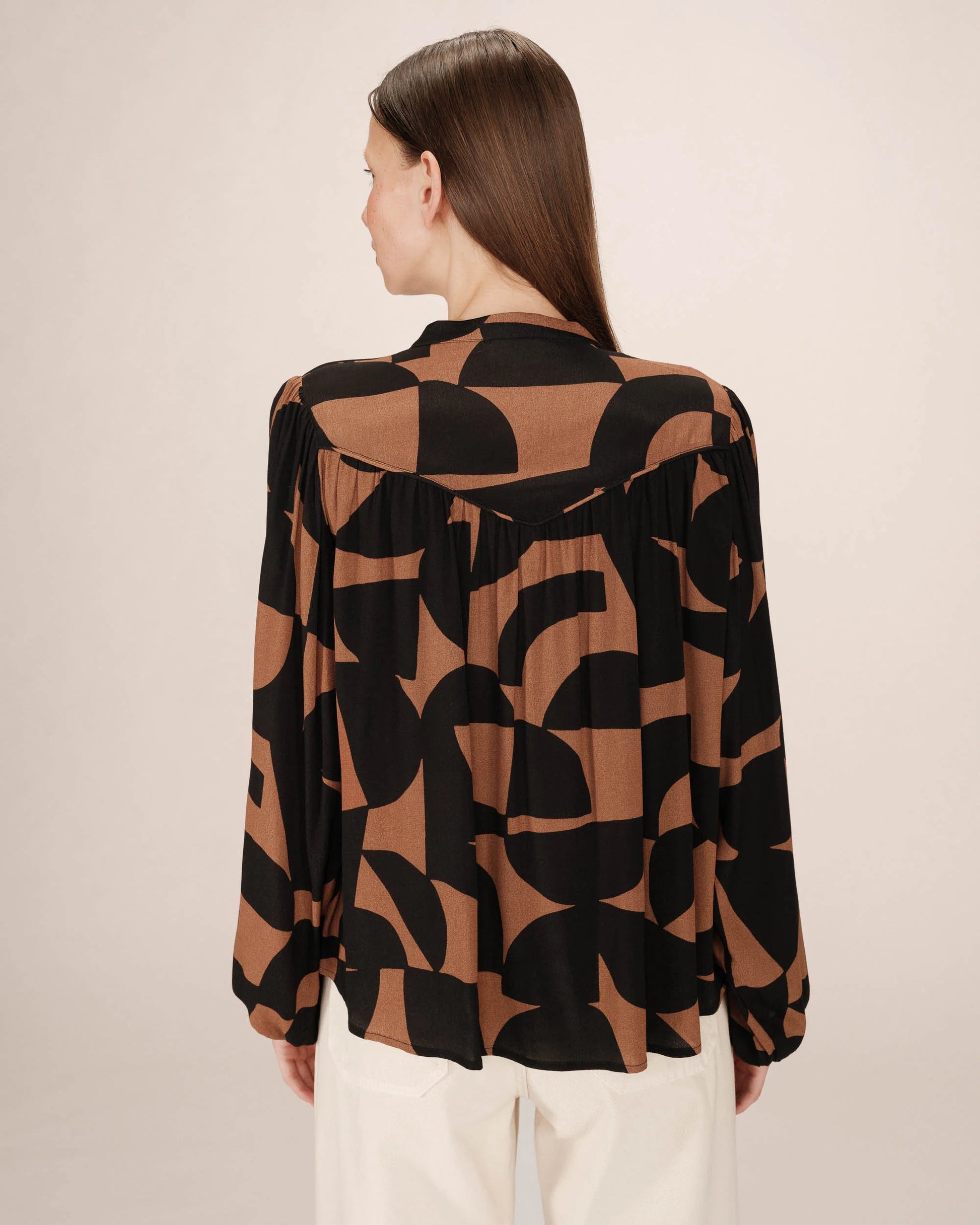 Woman wearing a black and brown patterned blouse against a beige background