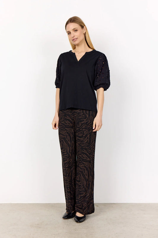 Woman wearing a black top and patterned pants against a white background