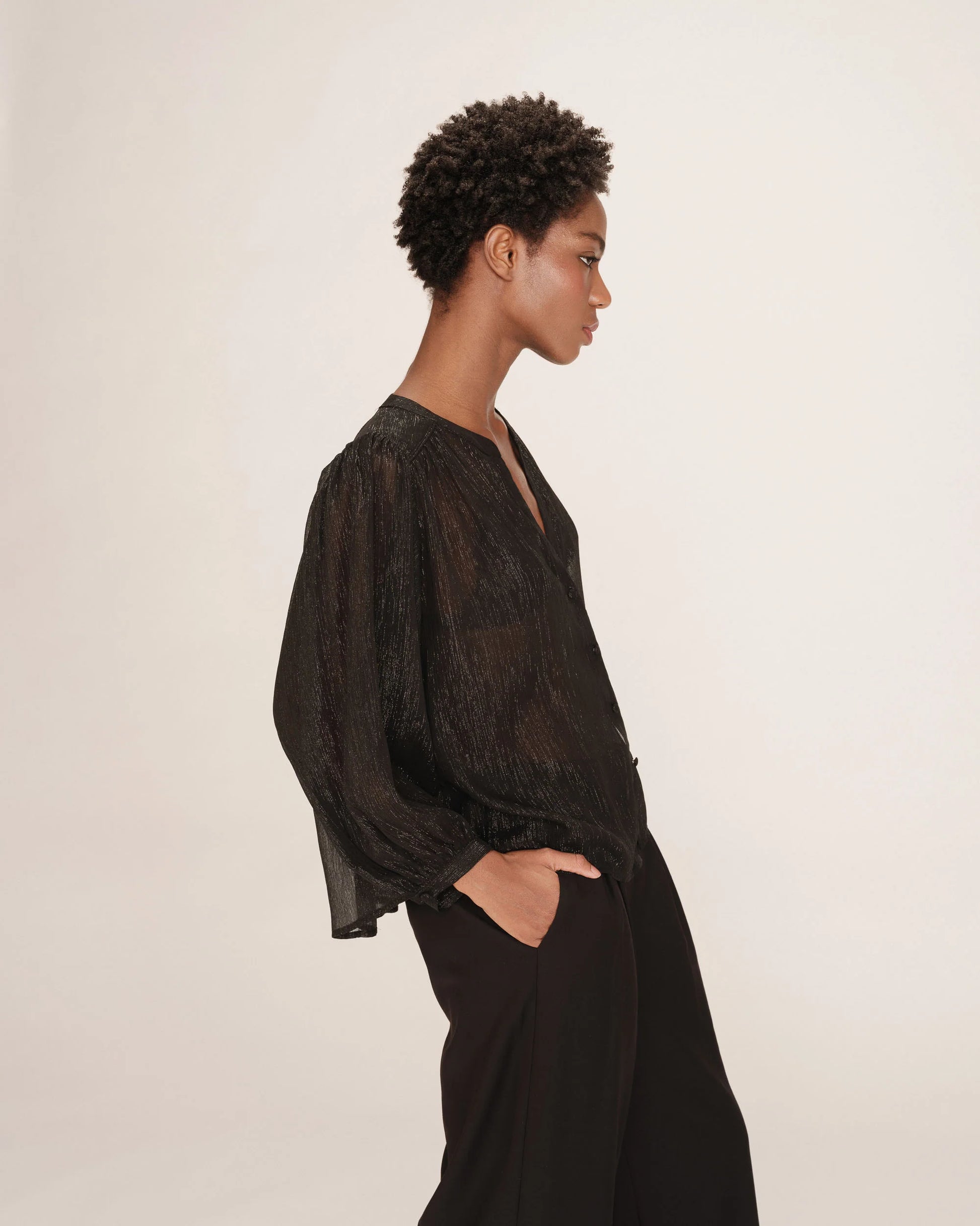 Woman wearing a dark blouse and pants against a plain background