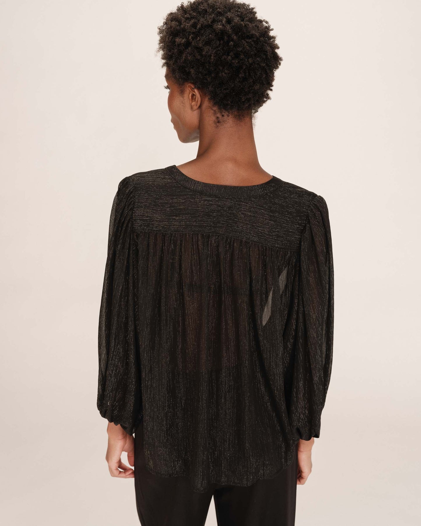 Person wearing a black textured blouse with long sleeves on a beige background