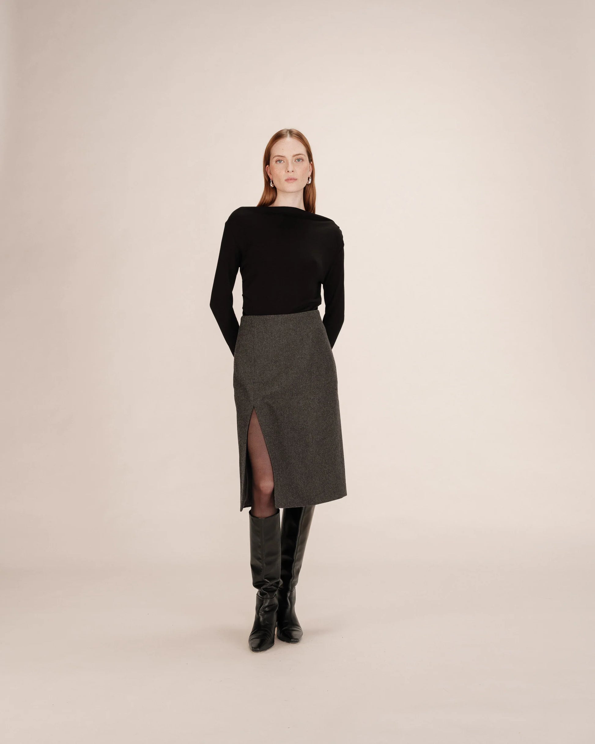 Woman wearing a black top and gray skirt with a slit on a beige background