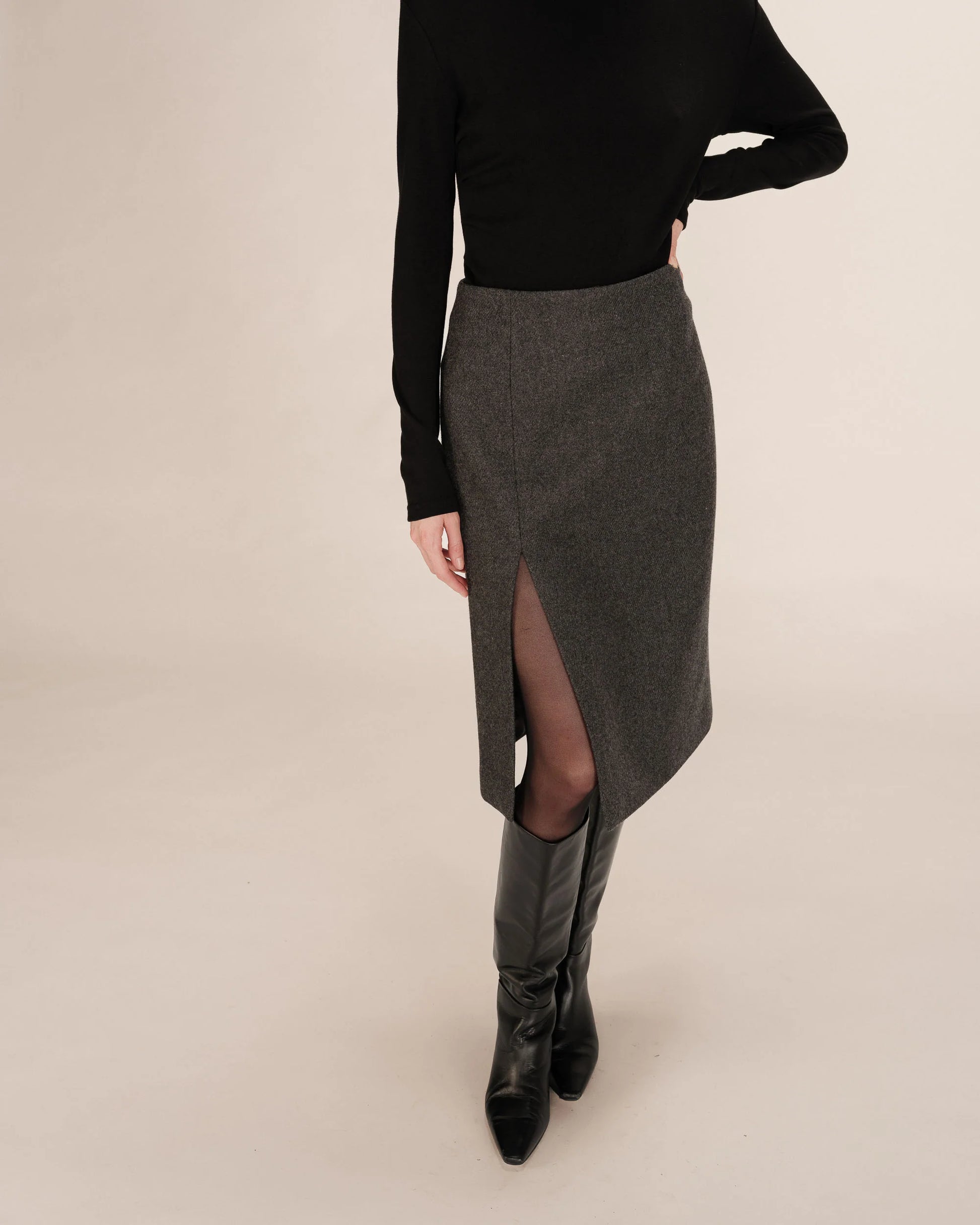 Person wearing a black top and gray skirt with a slit on a beige background