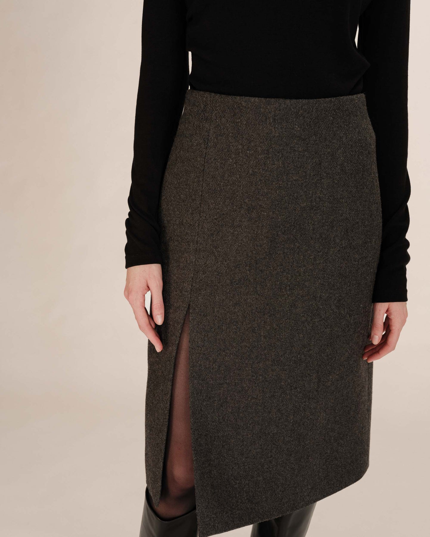 Person wearing a dark gray skirt with a front slit on a beige background