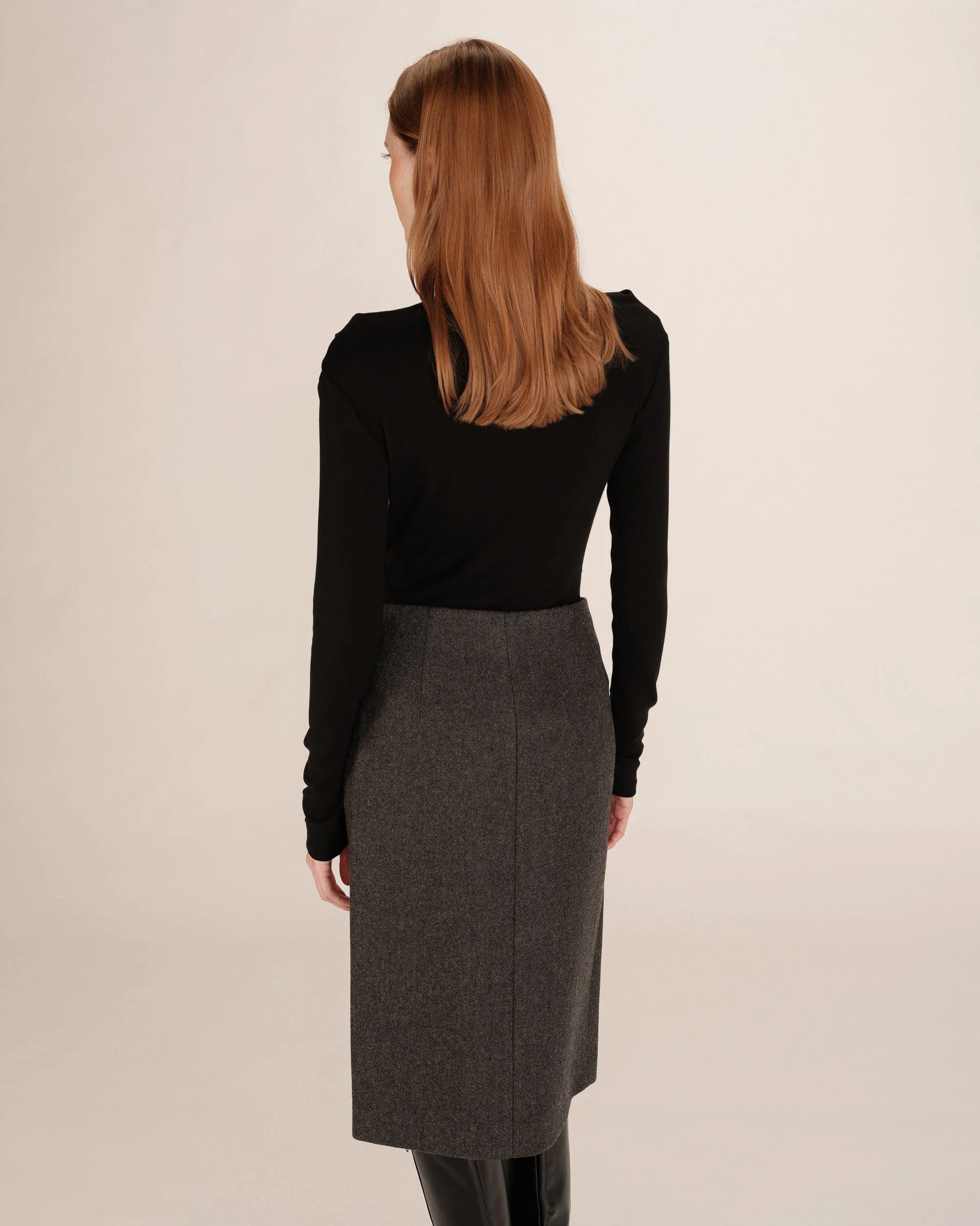 Woman wearing a black top and gray skirt on a beige background