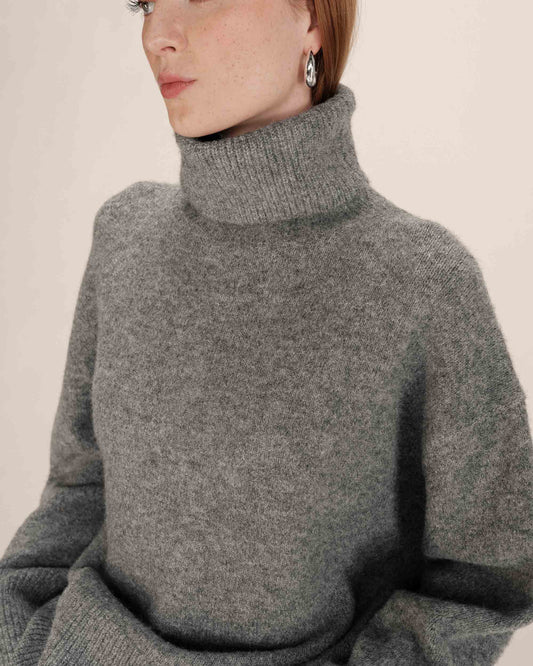 Person wearing a gray turtleneck sweater against a plain background