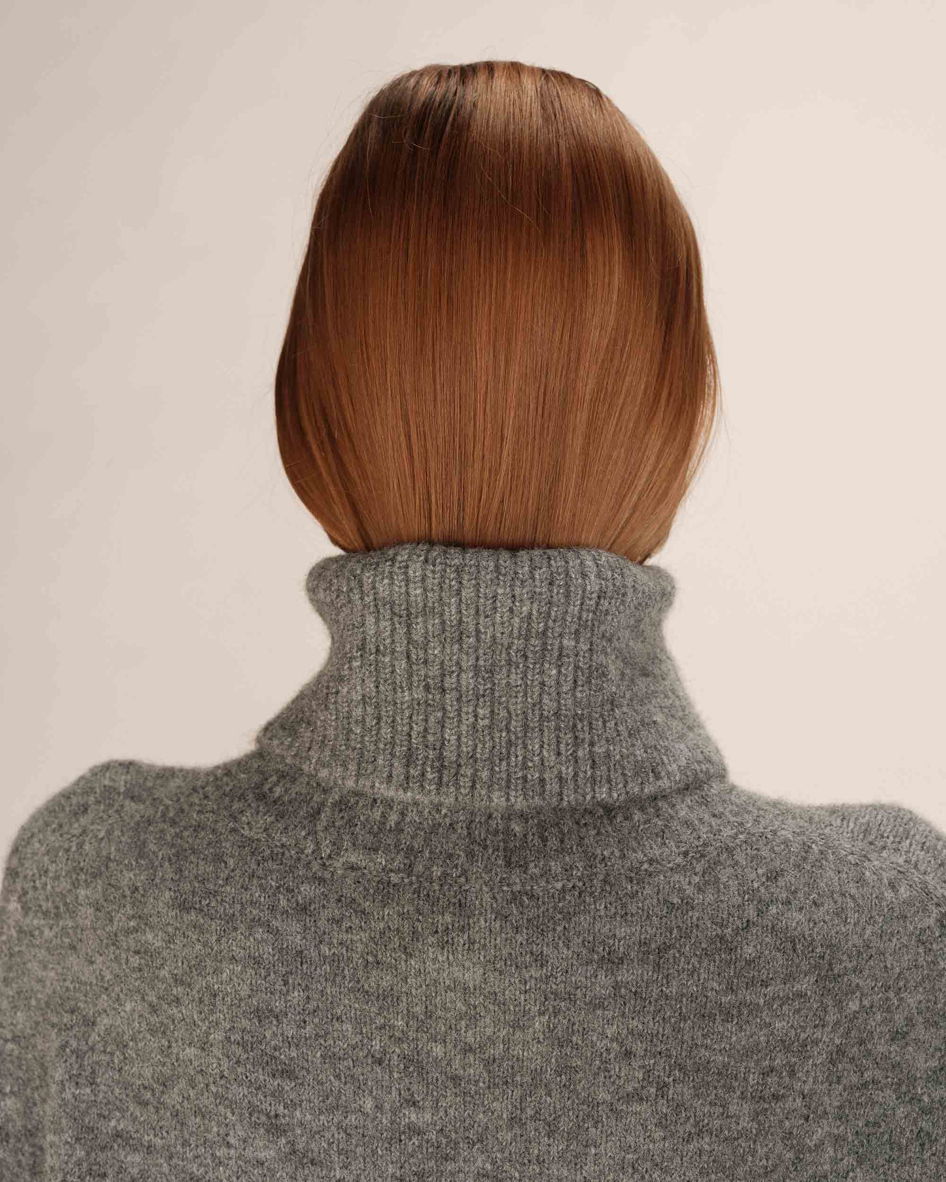 Person wearing a gray turtleneck sweater with a neutral background