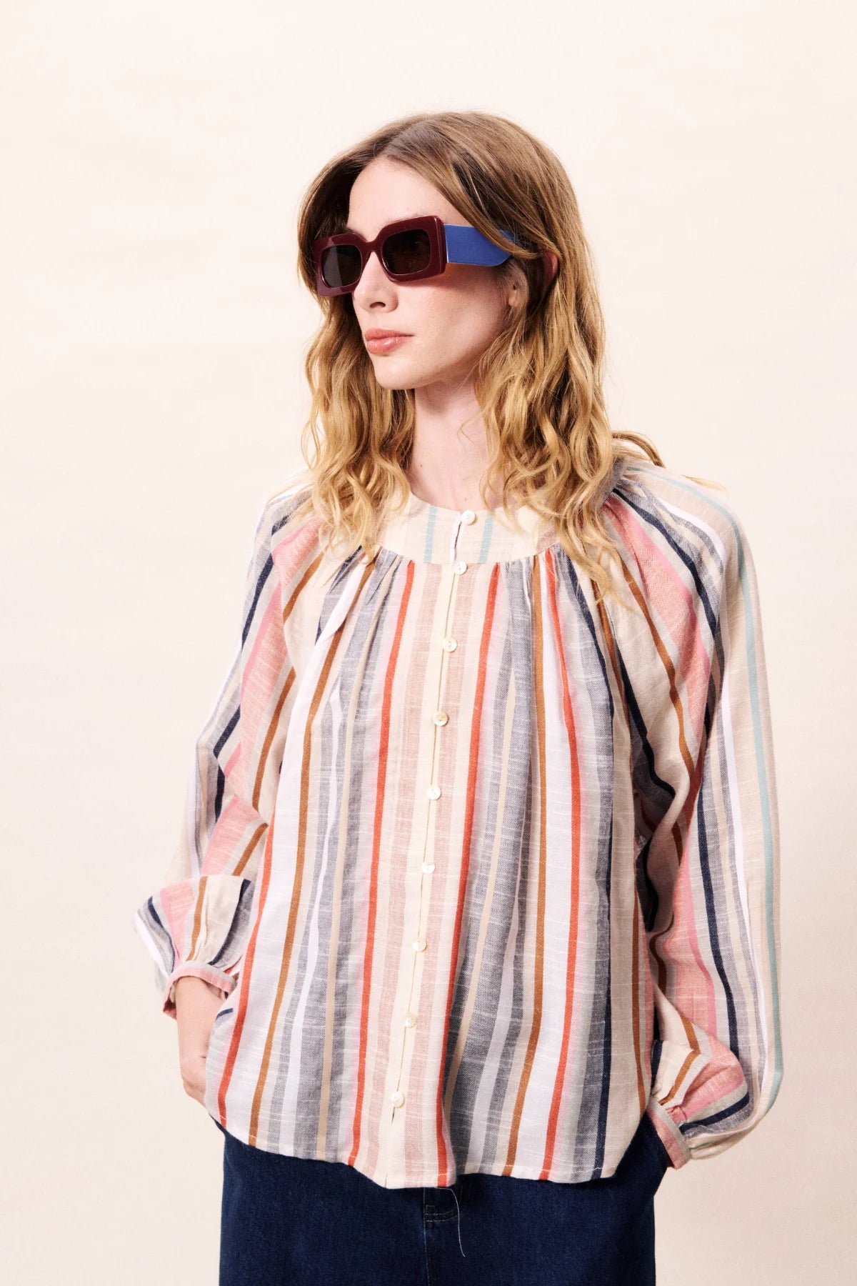 Woman wearing a colorful striped blouse and sunglasses against a plain background