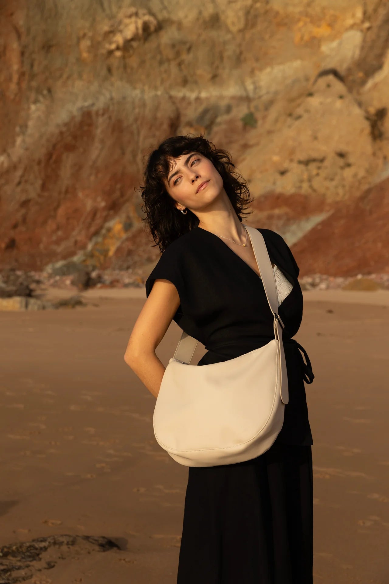 Woman in black dress with Cross body handbag in stone colour on a beach