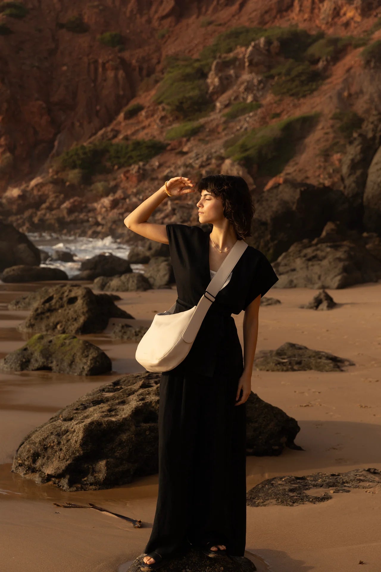 Woman in black dress with Cross body handbag in stone colour on a beach