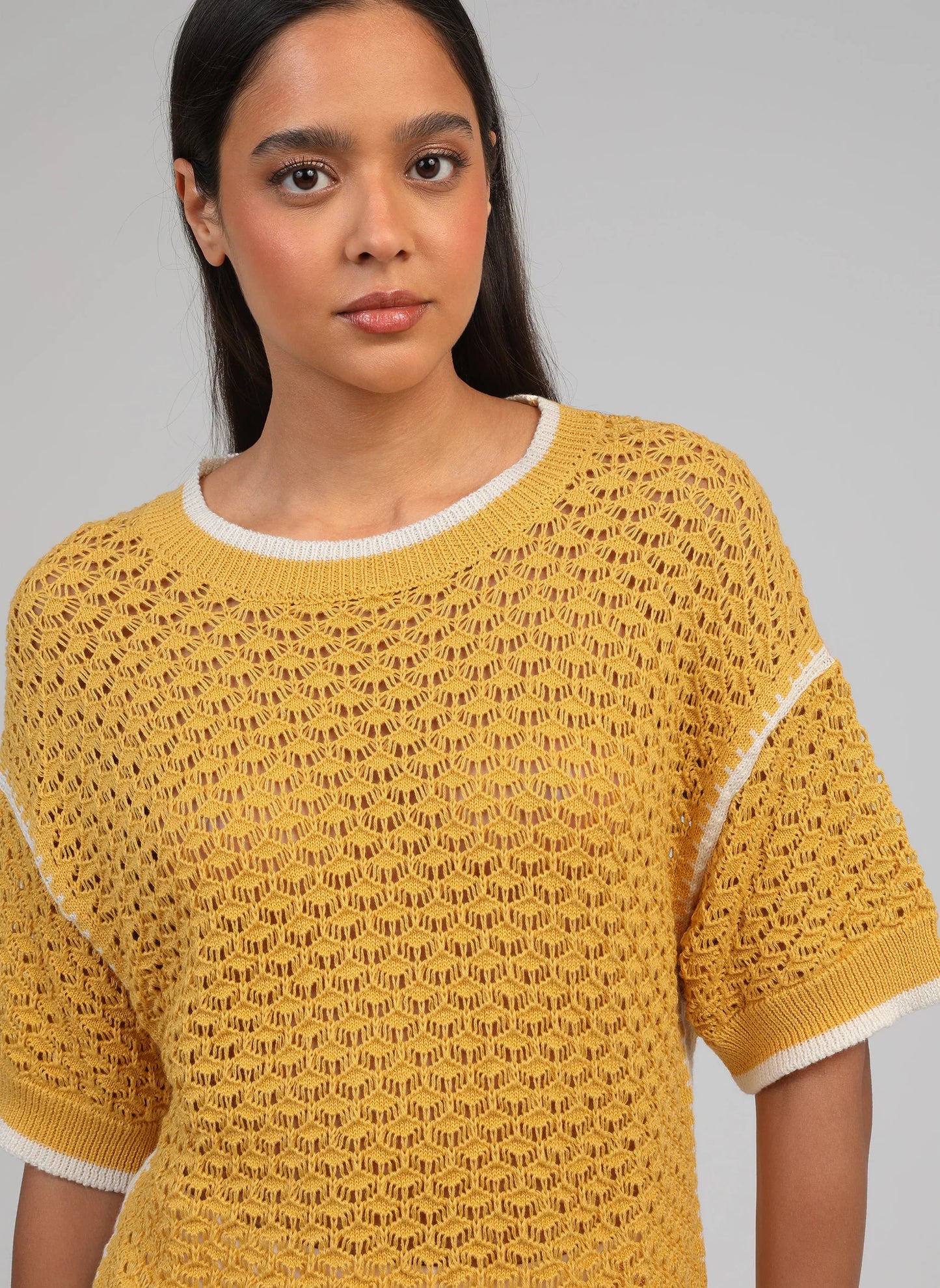 Woman wearing a yellow knit sweater against a gray background