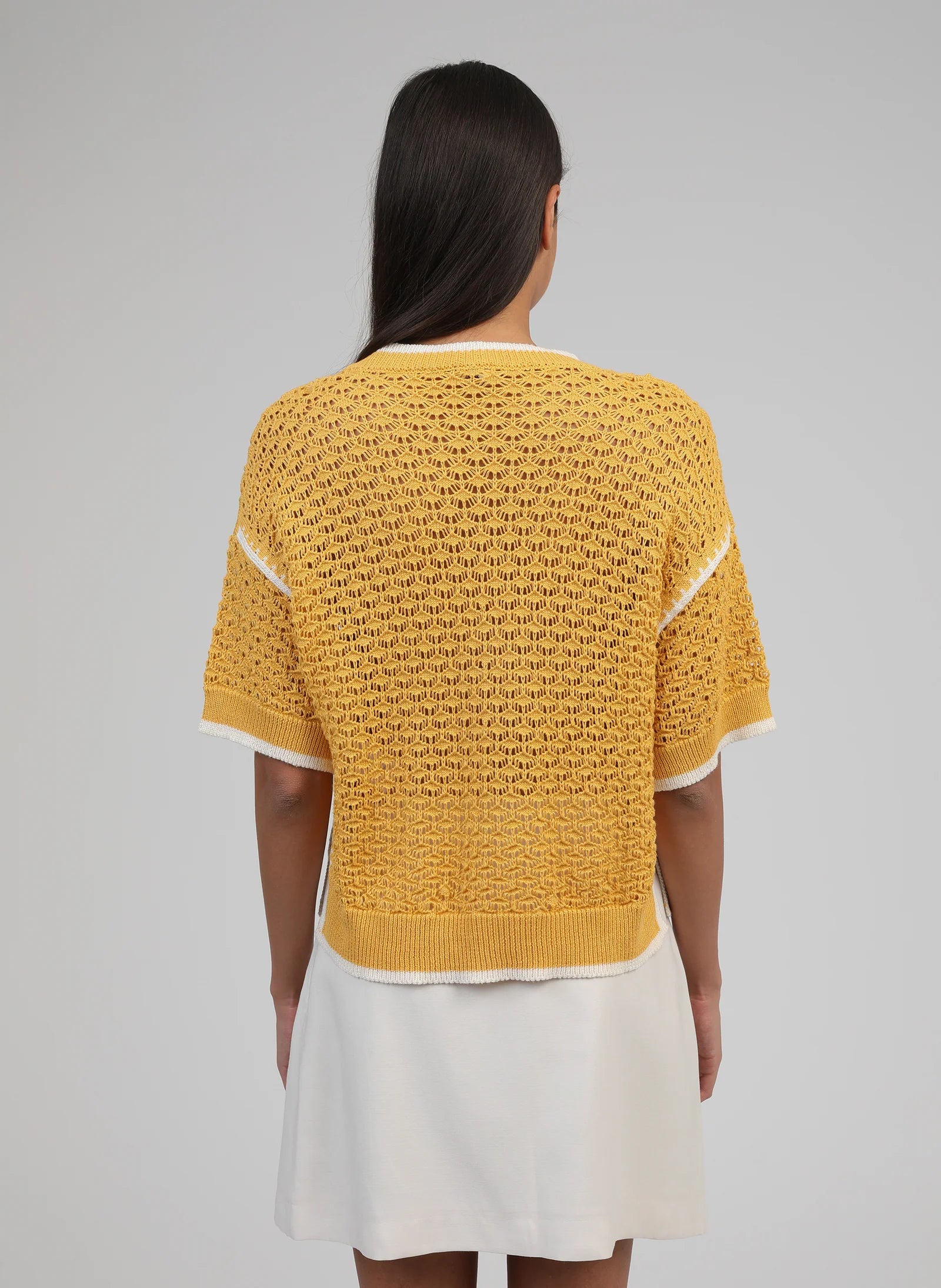 Person wearing a mustard yellow textured sweater over a white dress on a plain background