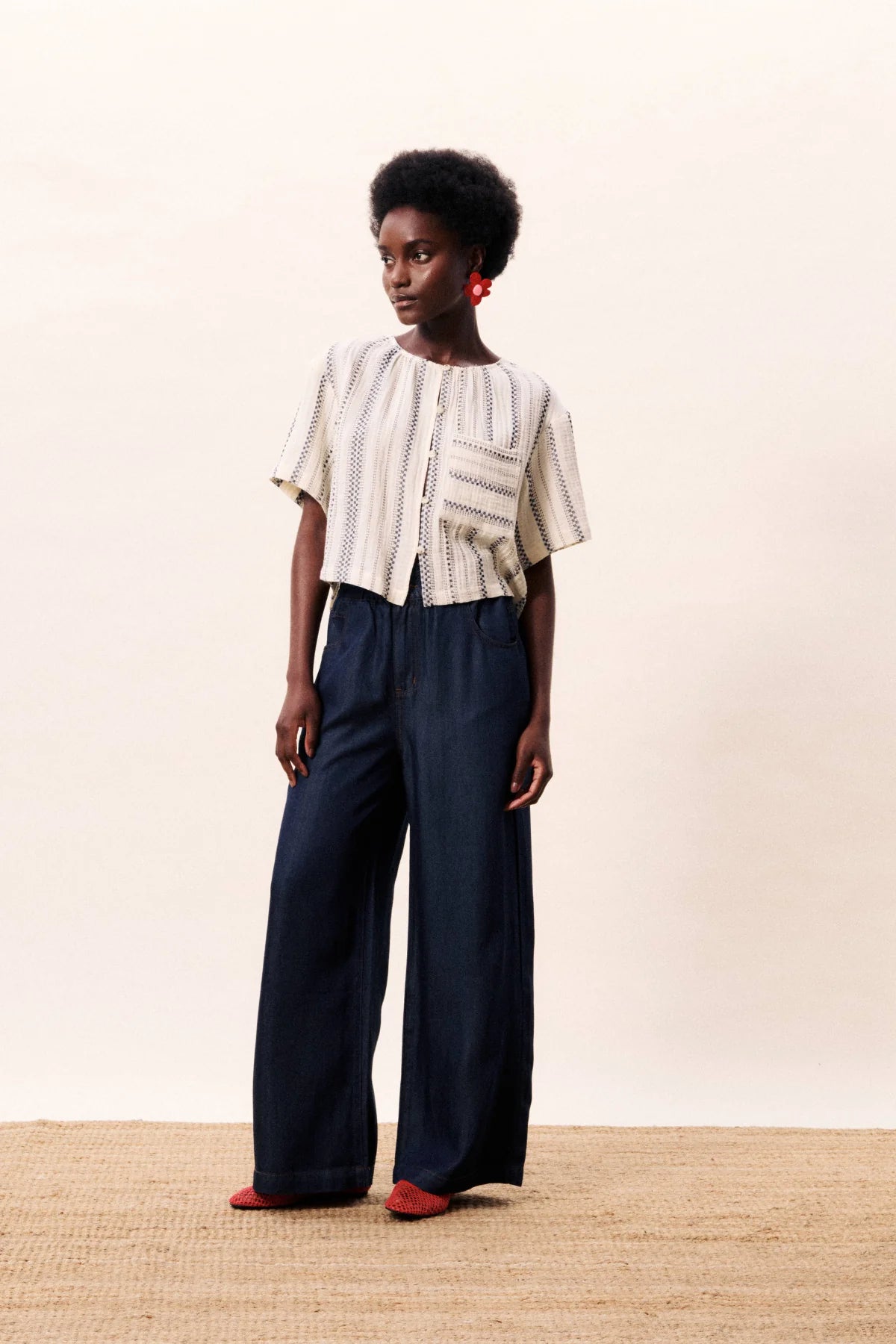 Woman wearing a white patterned top and dark blue pants on a beige background
