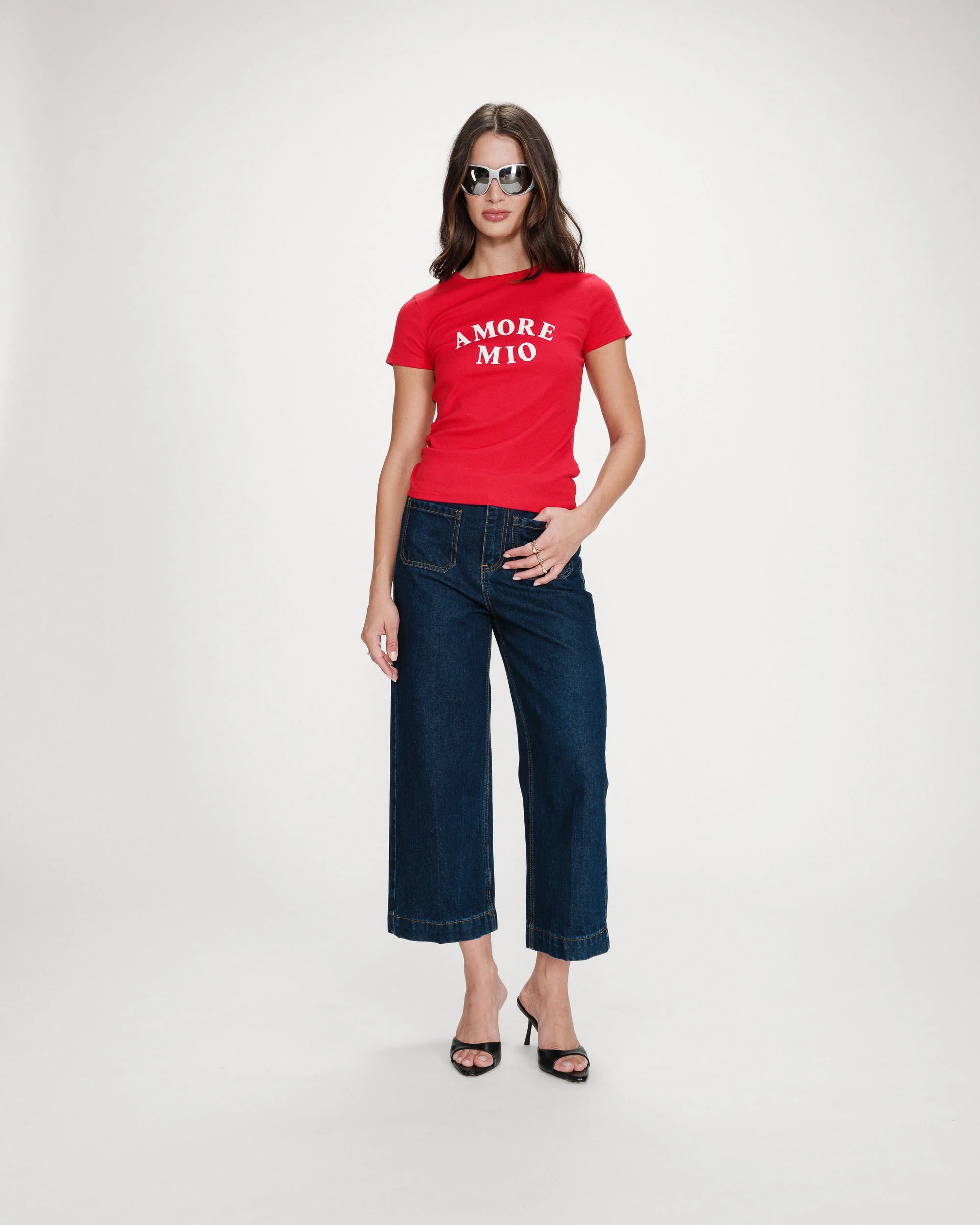 Woman wearing a red t-shirt with 'AMORE MIO' text and dark blue jeans on a white background