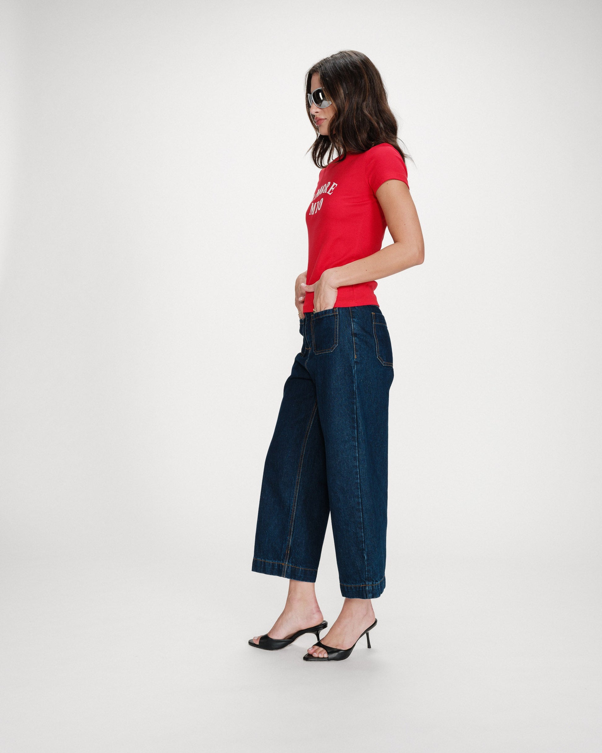 Woman wearing a red t-shirt and dark blue jeans on a white background