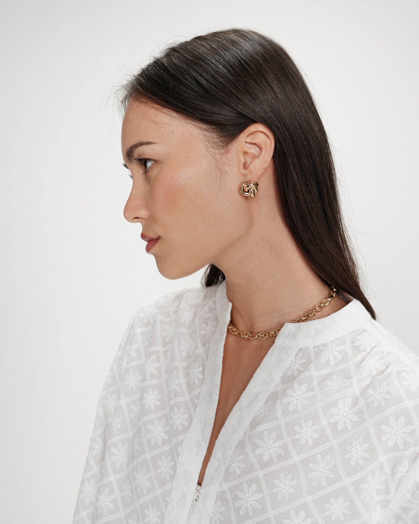 Woman wearing gold earrings and a necklace on a white background