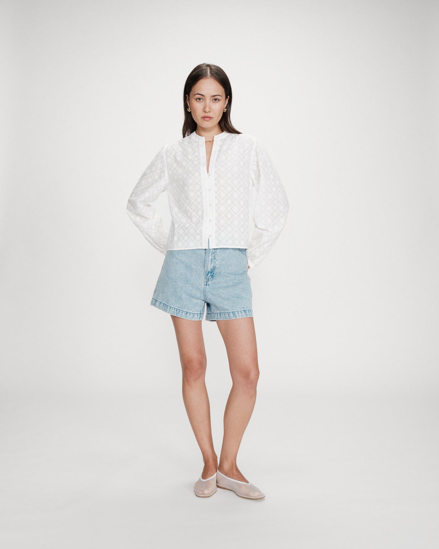 Woman wearing a white blouse and light blue denim shorts on a white background