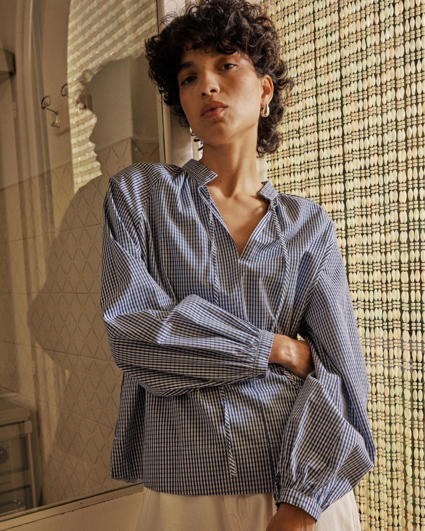 Woman wearing a blue checkered shirt standing in a room with a textured wall.