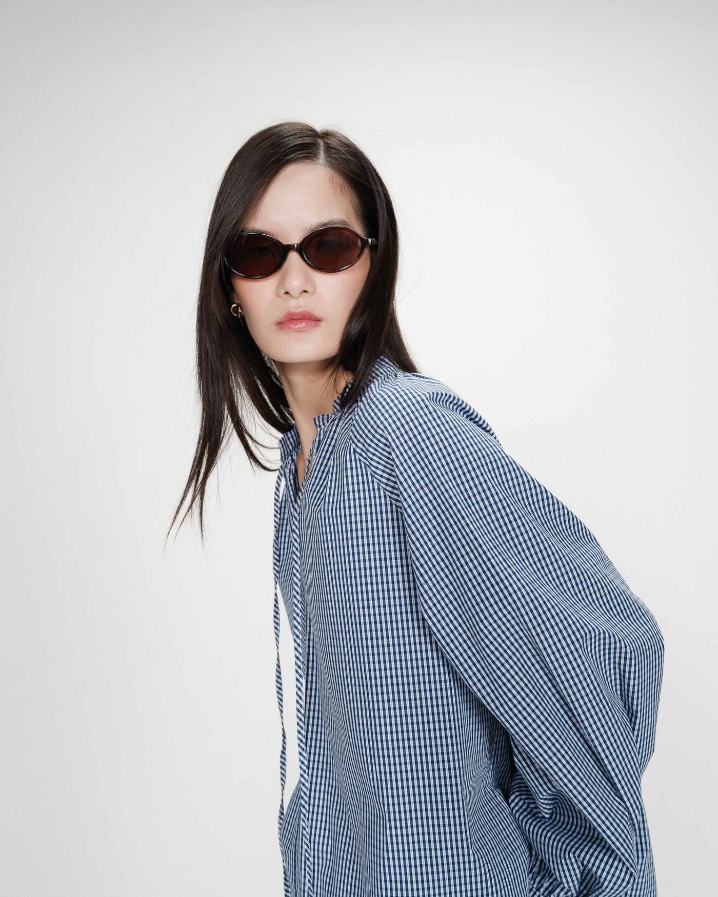 Woman wearing a blue checkered shirt and sunglasses on a white background