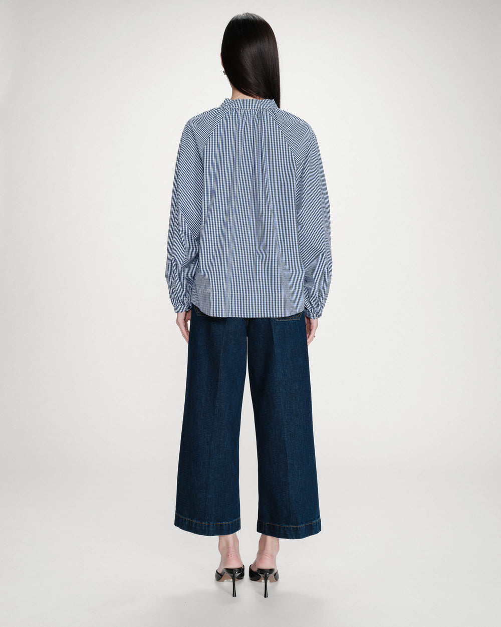 Person wearing a blue checkered shirt and dark jeans on a white background