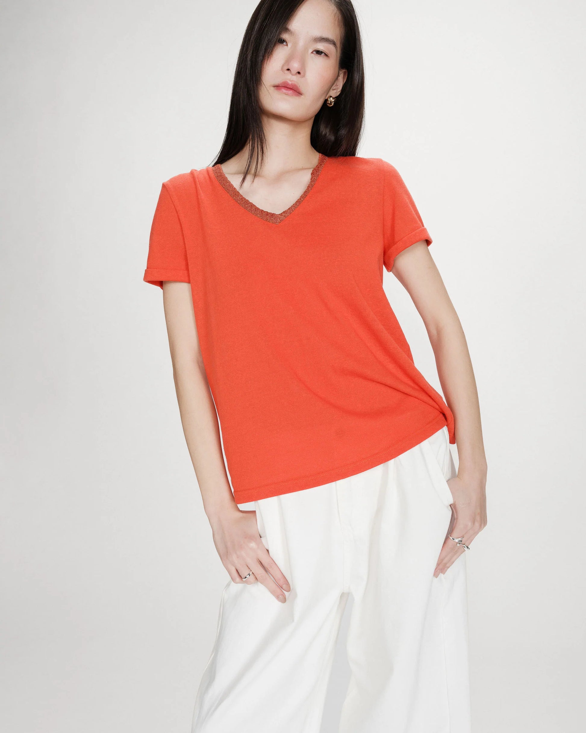 Woman wearing a bright orange t-shirt and white pants on a plain background