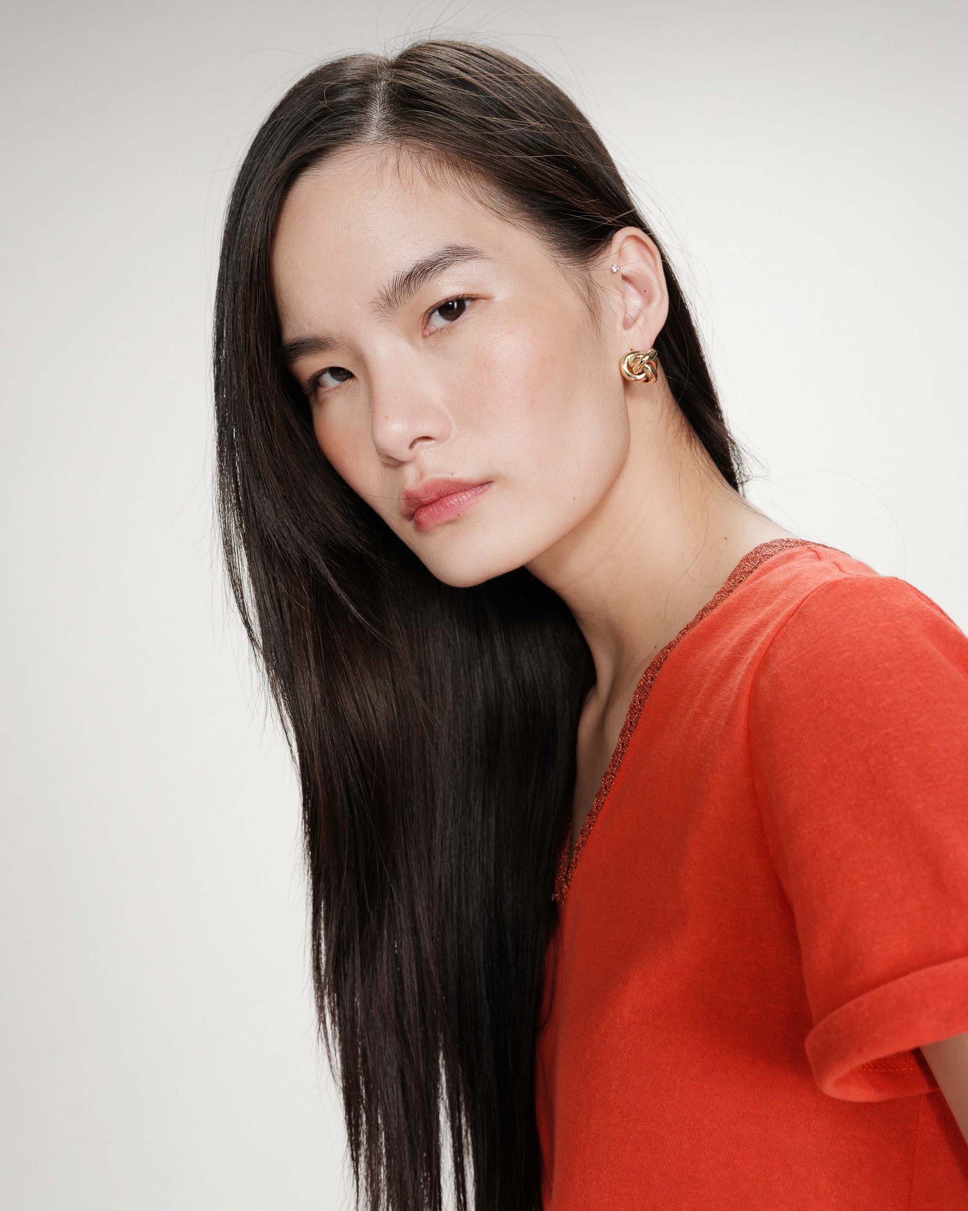 Woman with long dark hair wearing a red top against a plain background
