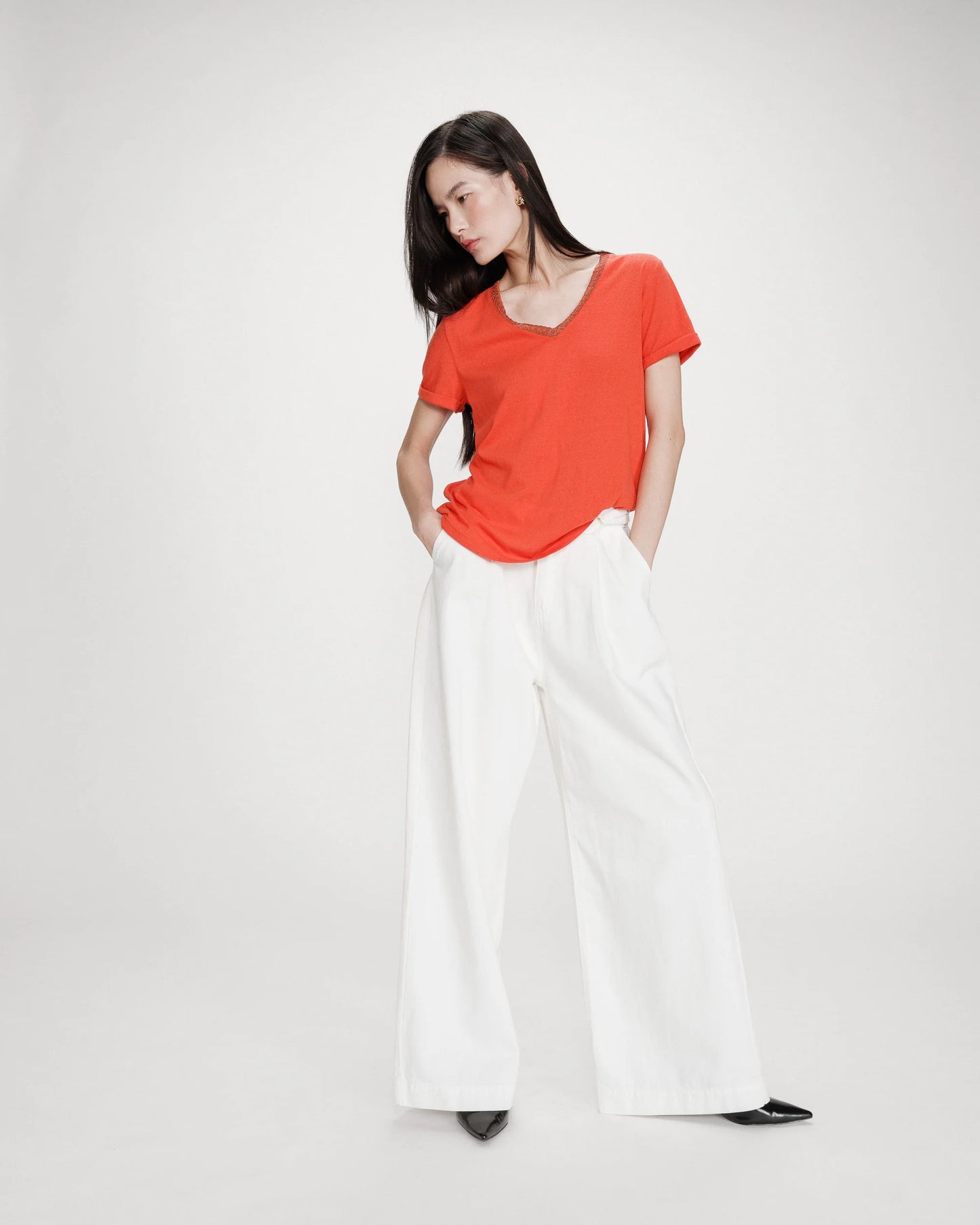 Woman wearing a bright orange top and white pants on a plain background