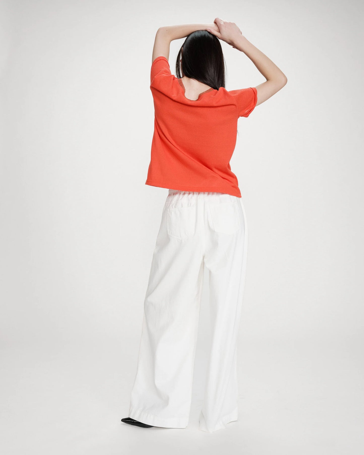 Person wearing an orange top and white pants on a plain background