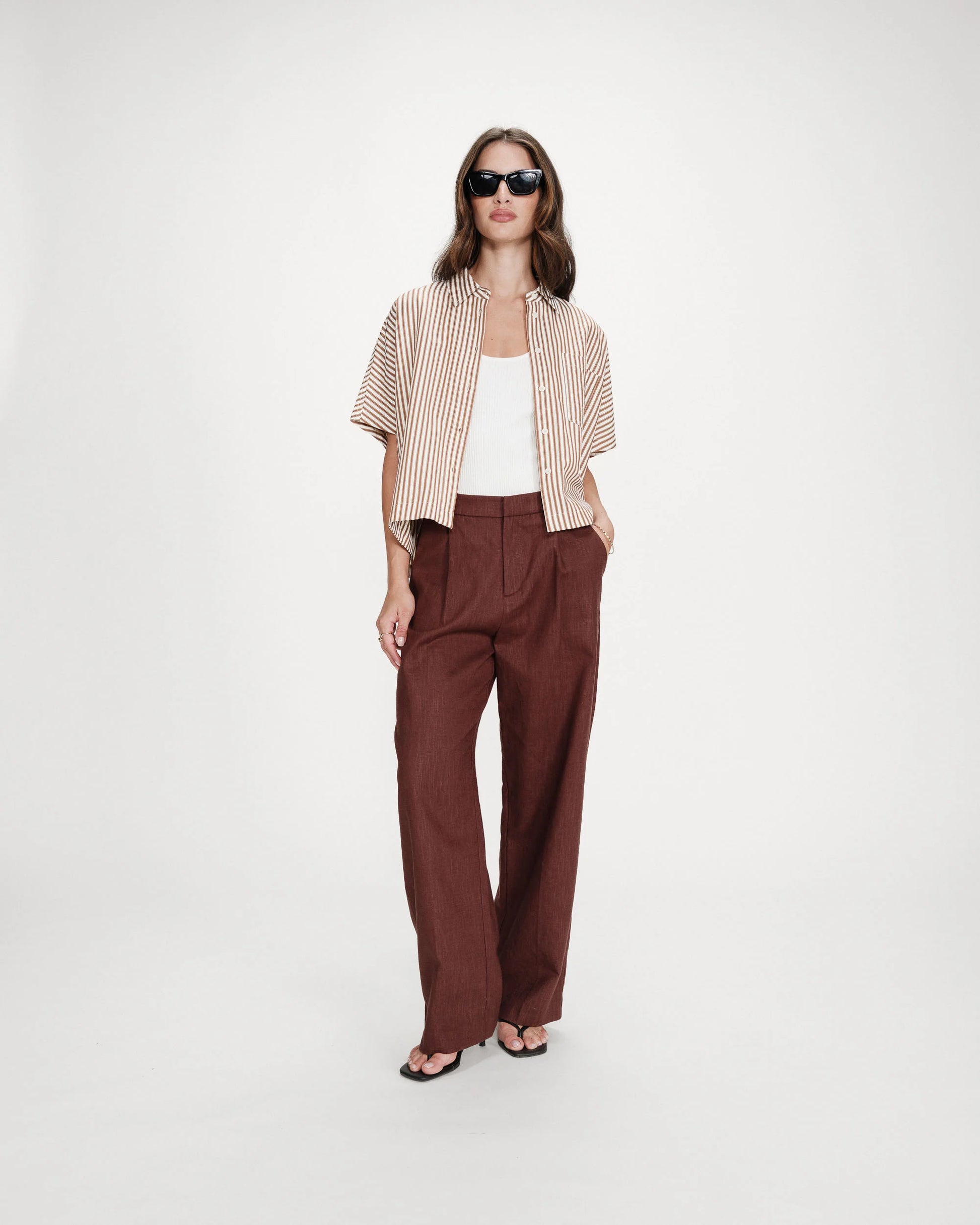Woman wearing a striped shirt, white top, and brown pants on a white background