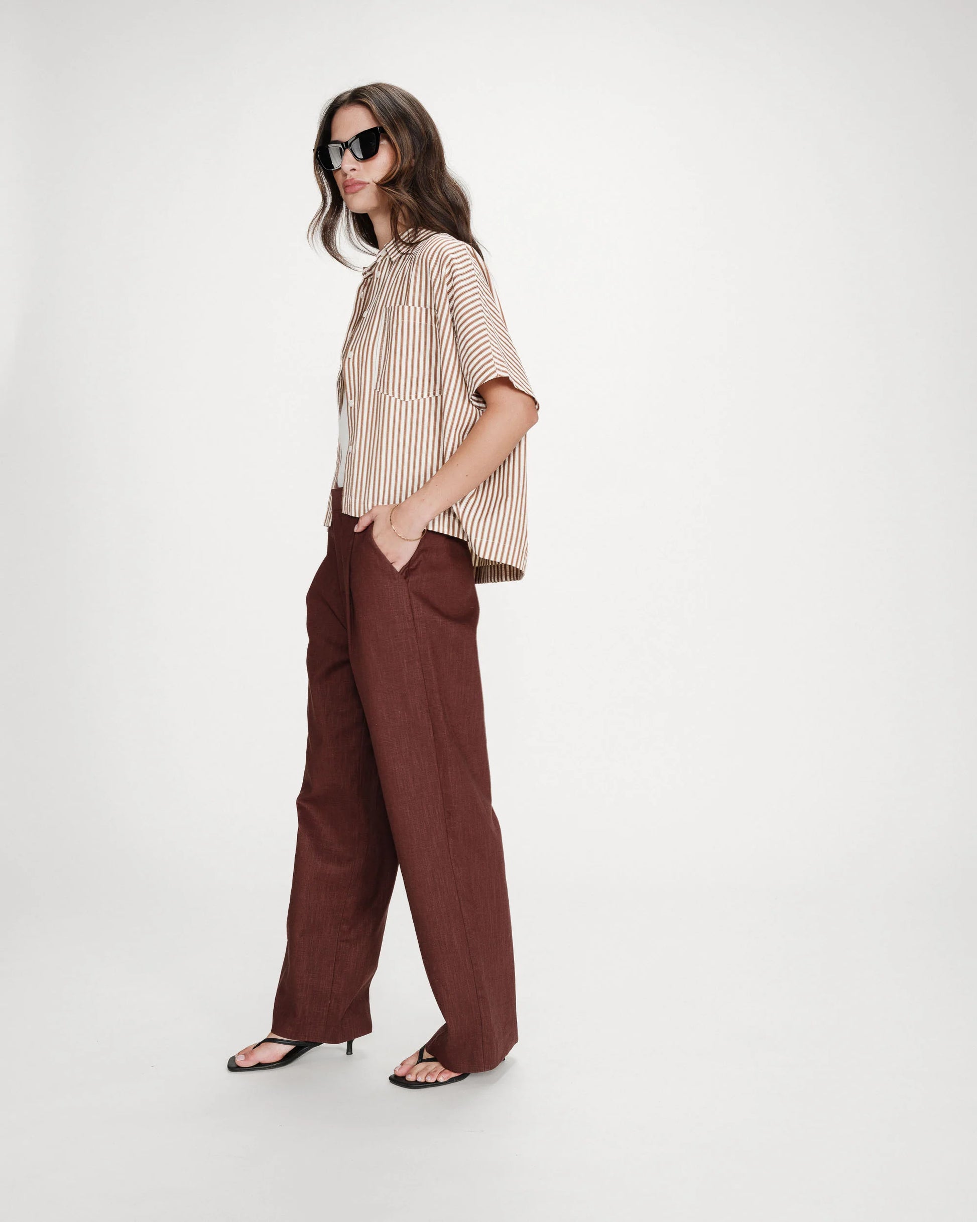Woman wearing a striped shirt and brown pants on a white background