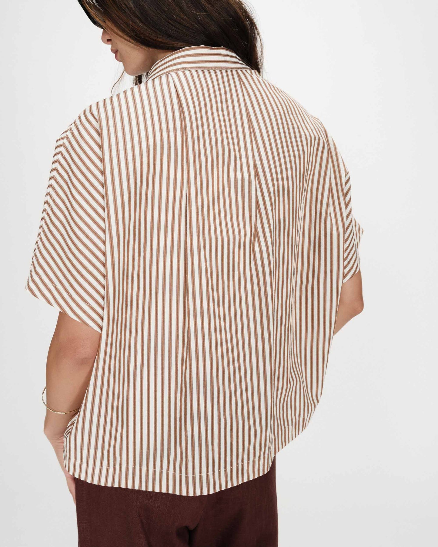 Person wearing a brown and white striped shirt on a plain background