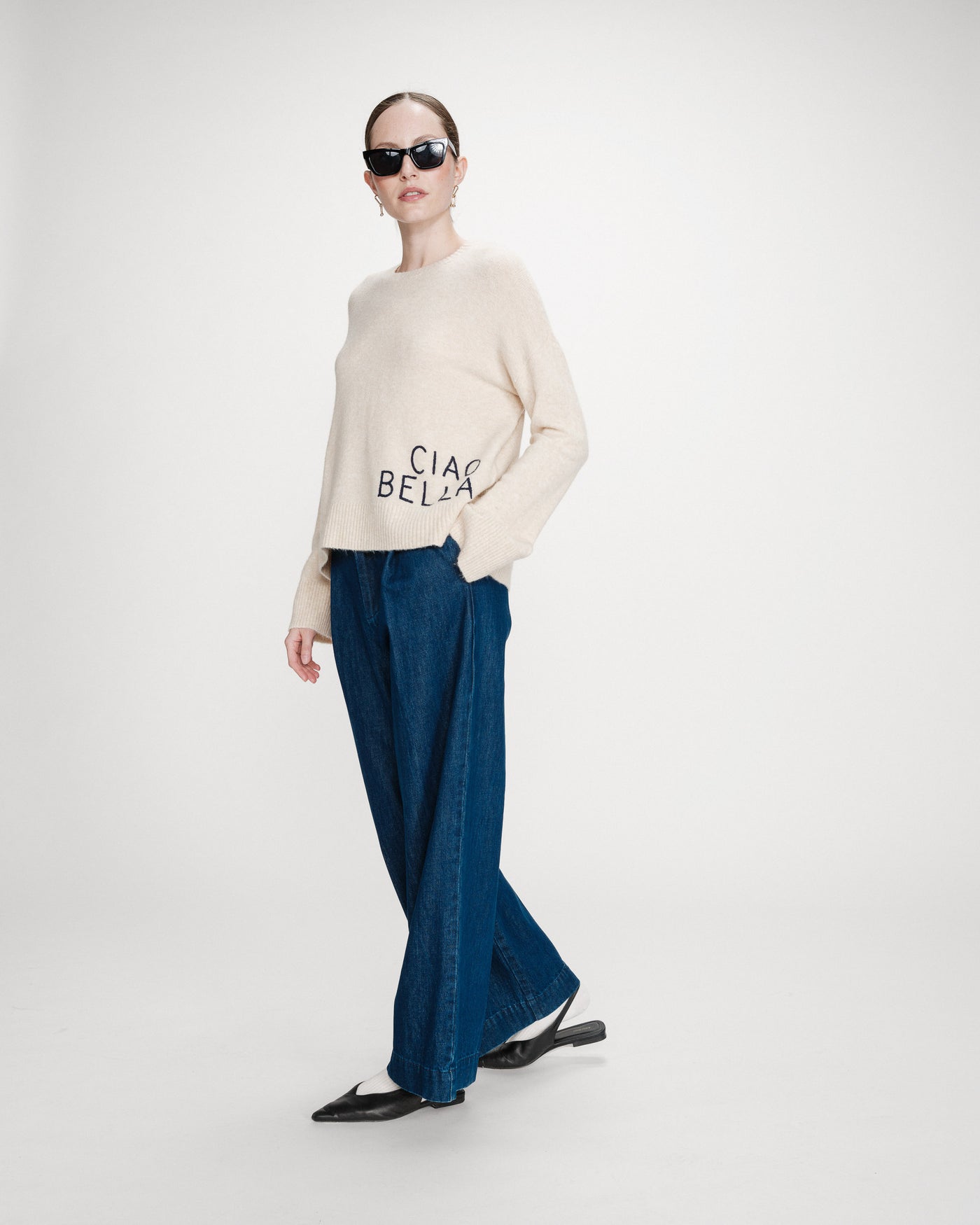 Person wearing a cream sweater with text and blue pants on a white background