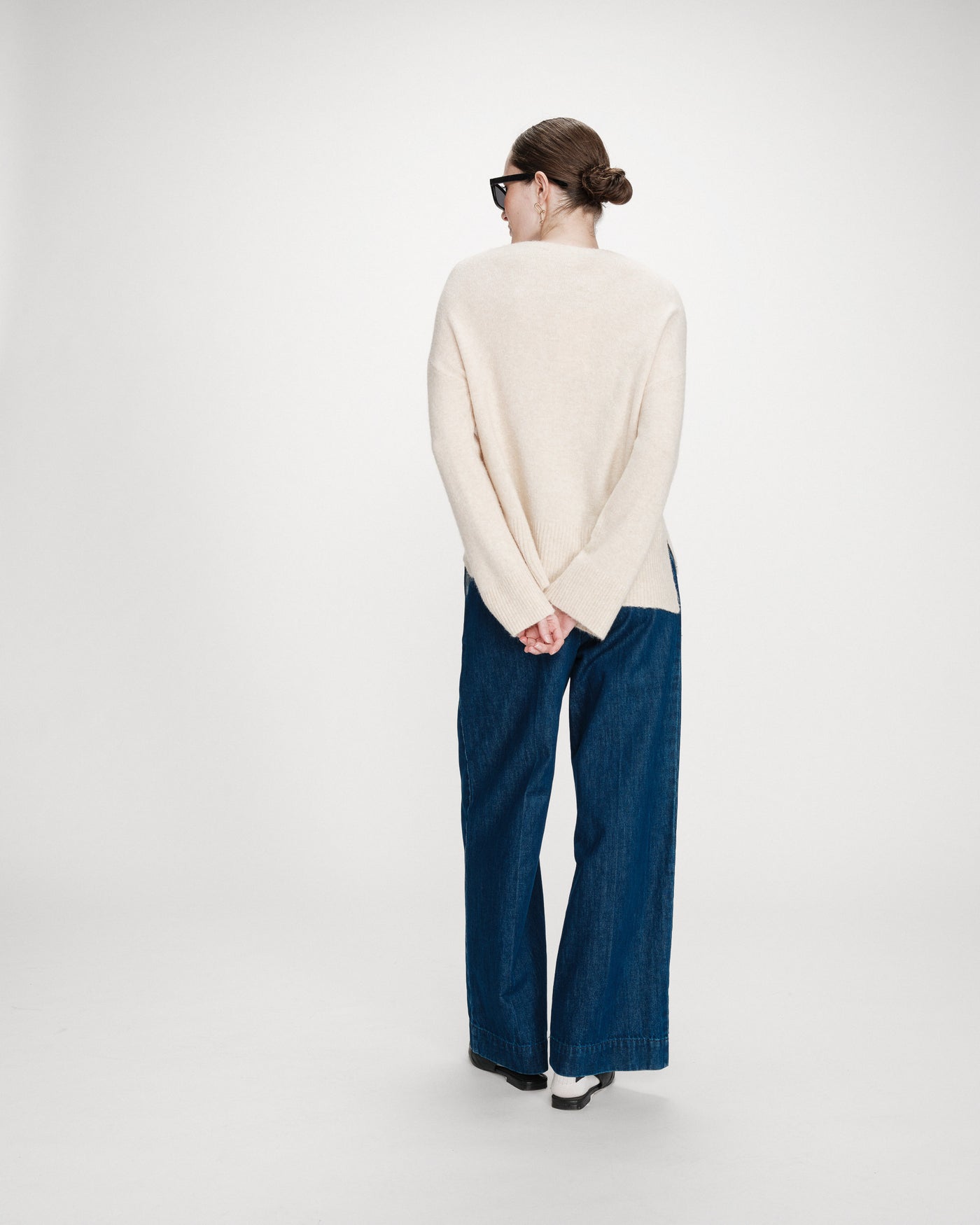 Person wearing a cream sweater and blue jeans on a white background