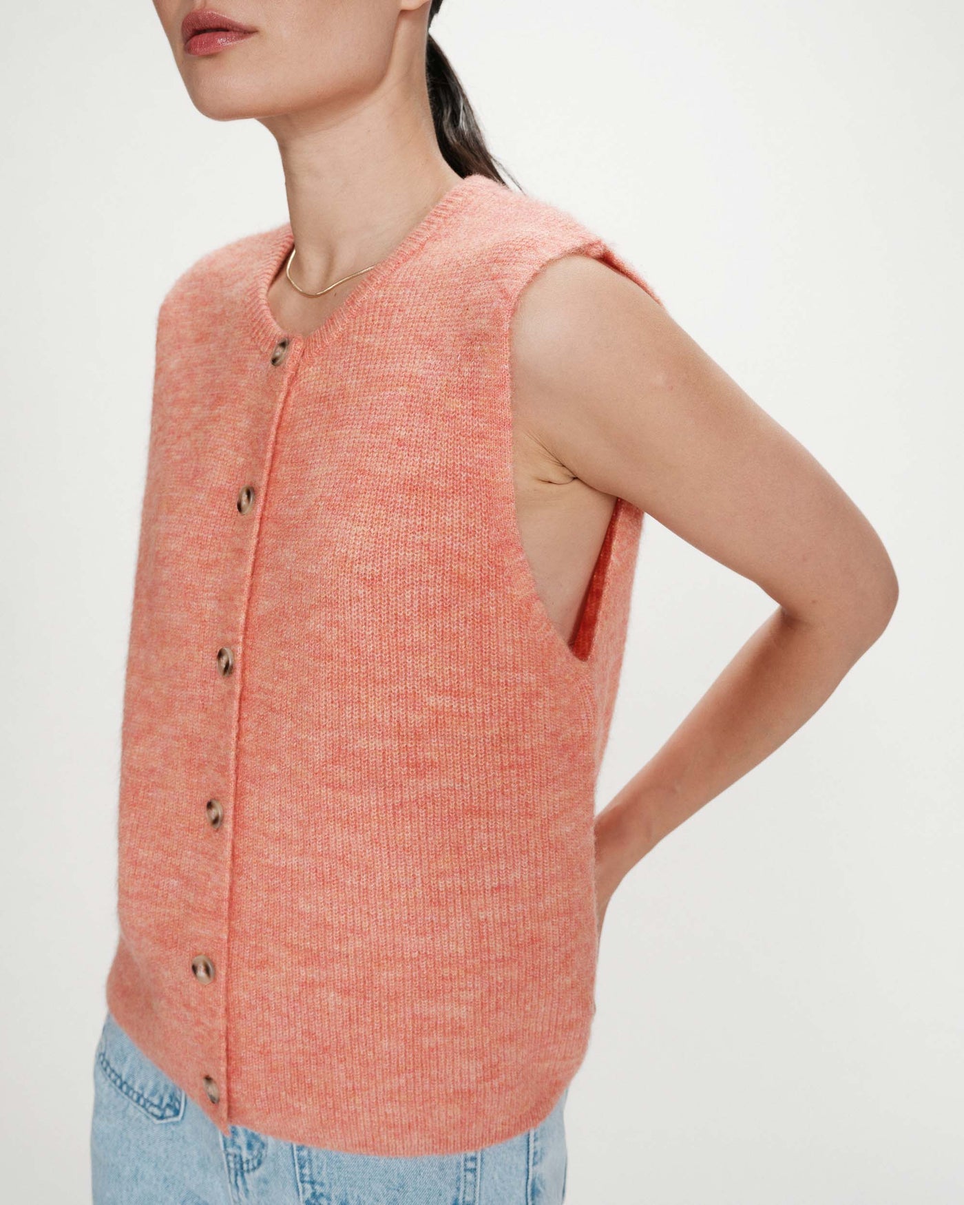 Woman wearing a pink sleeveless knitted vest on a plain background