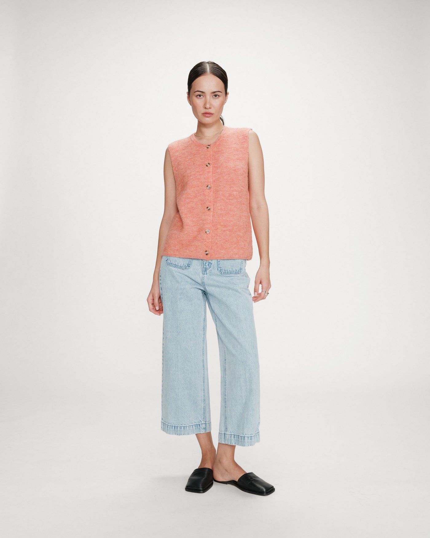 Woman wearing a sleeveless pink top and light blue jeans on a white background