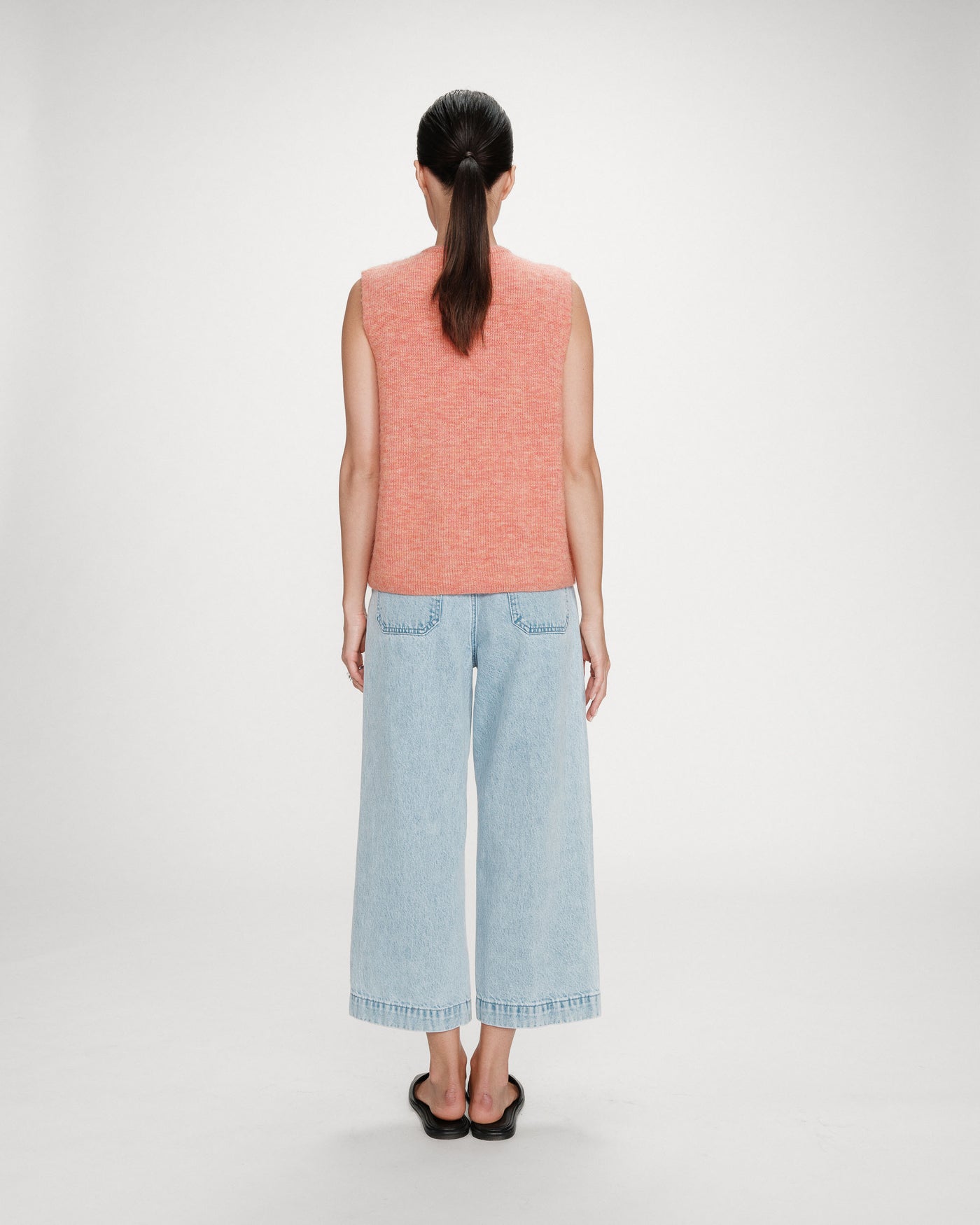 Person wearing a sleeveless pink top and light blue jeans on a white background