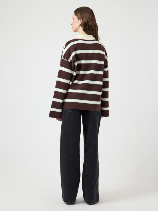 Person wearing a brown and white striped sweater with black pants on a white background