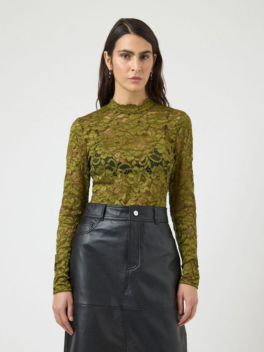 Woman wearing a green lace long sleeve top with a black leather skirt. Neutral background.