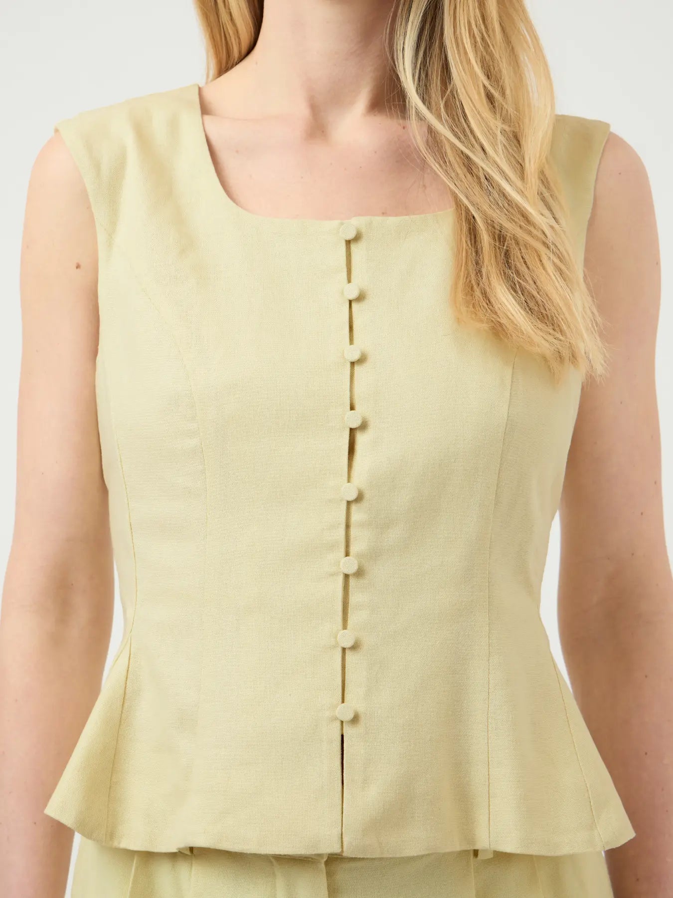 Light yellow sleeveless top with button details on a plain background